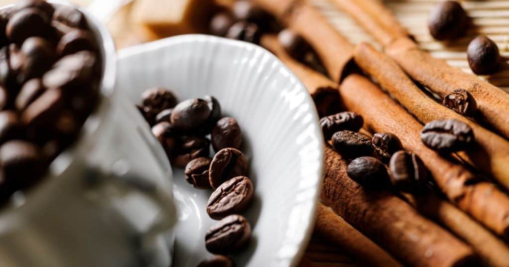 coffee beans and cinnamon sticks scattered around a white coffee cup and saucer